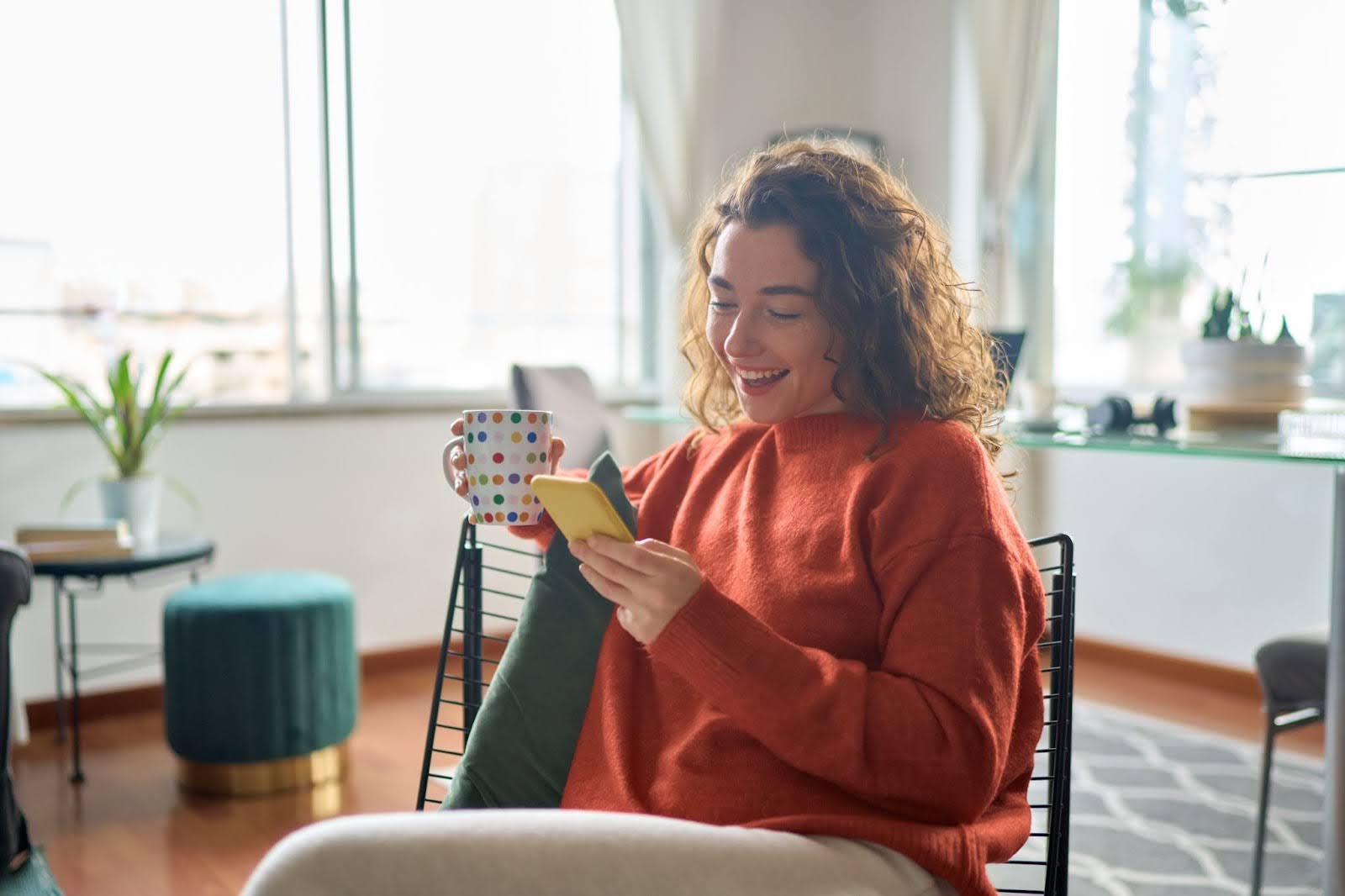 a young woman typing on your phone with a mug in her hand
